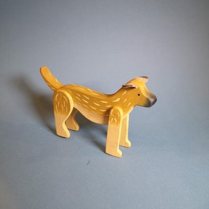 Pu&ograve; includere: Un cane giocattolo di legno dipinto in tonalit&agrave; gialle e marroni. Il cane ha una coda lunga e sta in piedi su tutte e quattro le zampe.