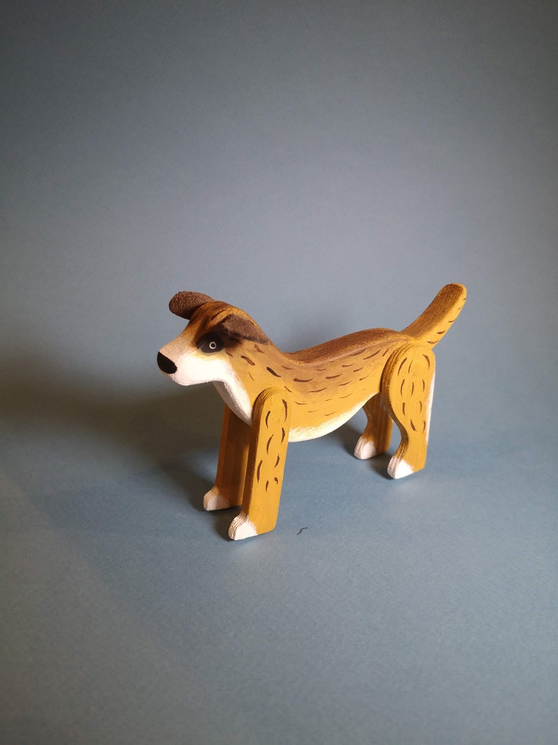 Pu&ograve; includere: Un cane di legno giocattolo dipinto di marrone e bianco. Il cane ha una coda lunga e sta in piedi su tutte e quattro le zampe.