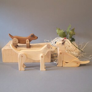 Pu&ograve; includere: Tre figurine di cane in legno, due sono di colore marrone chiaro e una &egrave; di colore marrone scuro. I cani sono tutti in pose diverse, uno &egrave; in piedi, uno &egrave; seduto e uno &egrave; sdraiato. Le figurine sono in legno e hanno una finitura naturale.