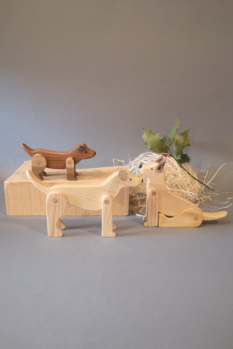Pu&ograve; includere: Tre figurine di cane in legno, due sono di colore marrone chiaro e una &egrave; di colore marrone scuro. I cani sono tutti in pose diverse, uno &egrave; in piedi, uno &egrave; seduto e uno &egrave; sdraiato. Le figurine sono in legno e hanno una finitura naturale.