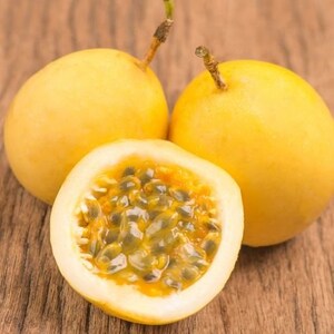 May include: Three yellow passion fruits, one cut open to reveal the seeds inside. The fruit is on a wooden surface.
