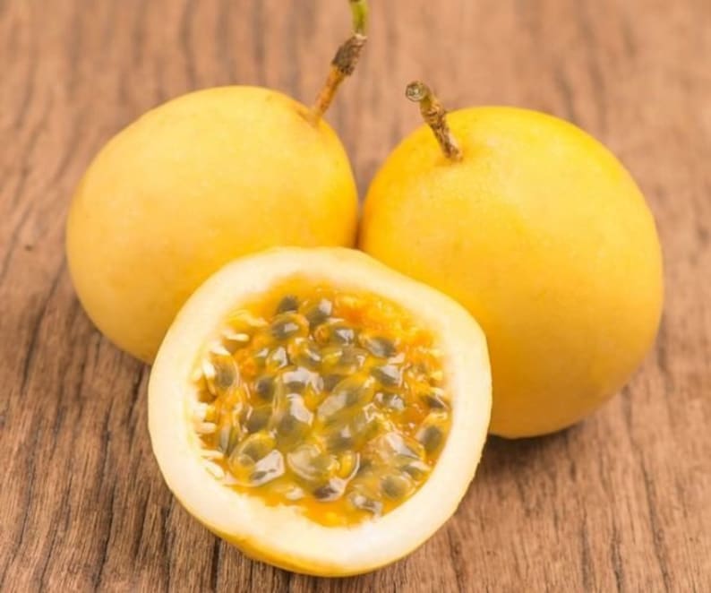 May include: Three yellow passion fruits, one cut open to reveal the seeds inside. The fruit is on a wooden surface.