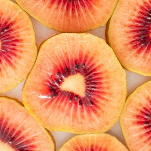 May include: Close-up of several slices of red-fleshed kiwi fruit. The kiwi fruit has a yellow outer skin and a bright red flesh with black seeds.