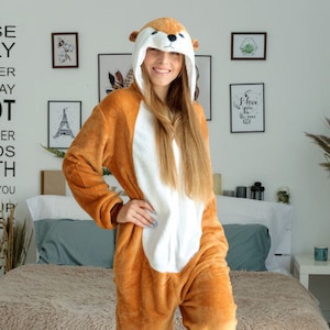 May include: A brown and white plush animal onesie with a hood featuring a squirrel face. The onesie has a zipper down the front and a long tail.