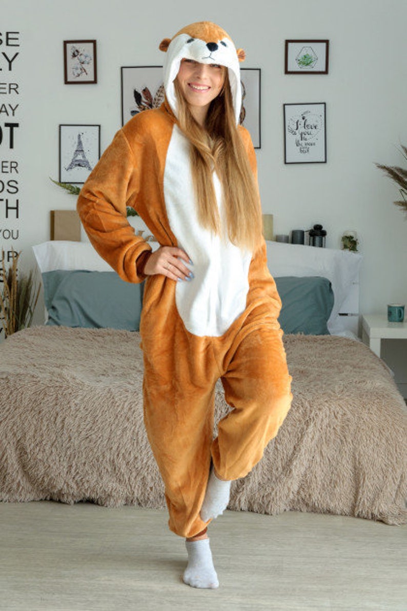 May include: A brown and white plush animal onesie with a hood featuring a squirrel face. The onesie has a zipper down the front and a long tail.