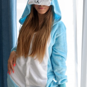 May include: A light blue hooded onesie with a white and blue animal face on the hood. The onesie has a white front panel and long sleeves.