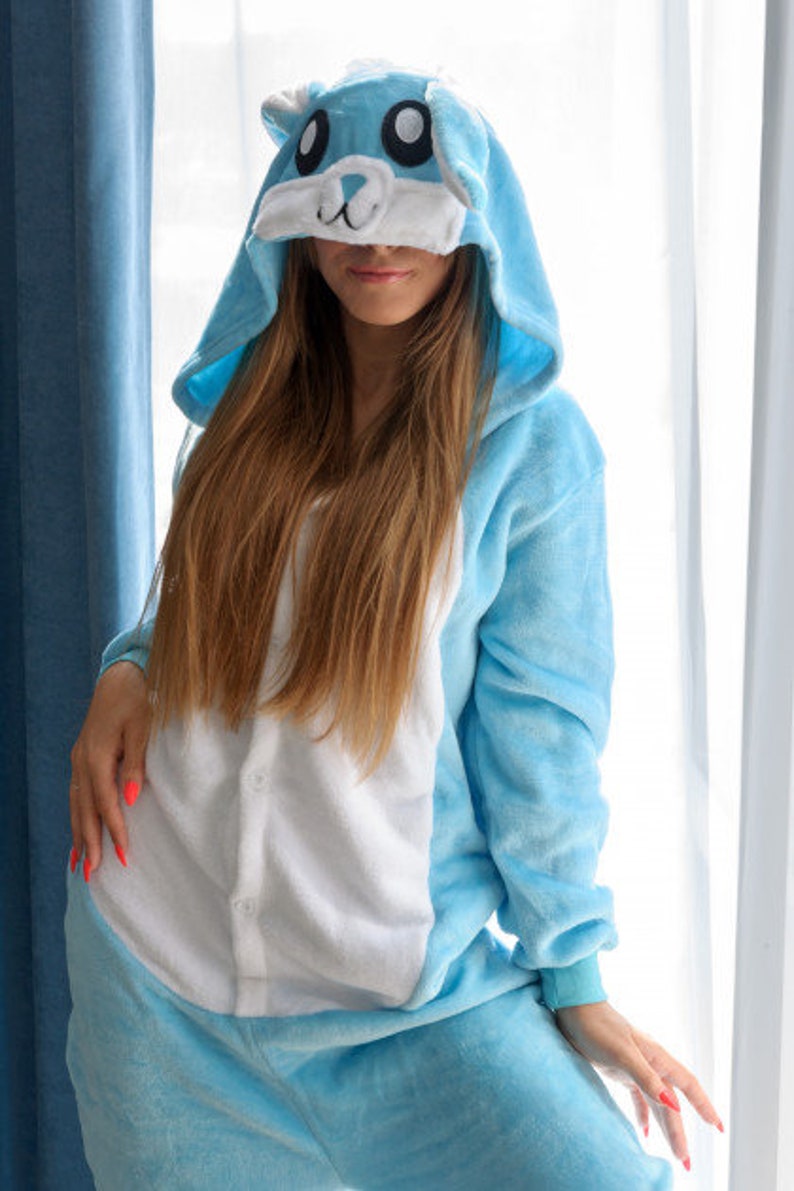 May include: A light blue hooded onesie with a white and blue animal face on the hood. The onesie has a white front panel and long sleeves.