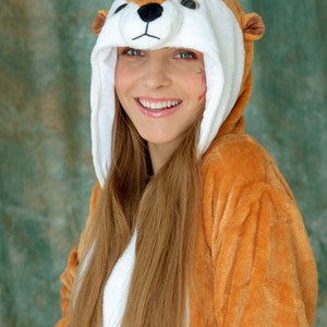 May include: A young person wearing a brown and white furry animal costume with a long, blonde ponytail. The costume has a large, round head with a white face and black eyes. The person is smiling.