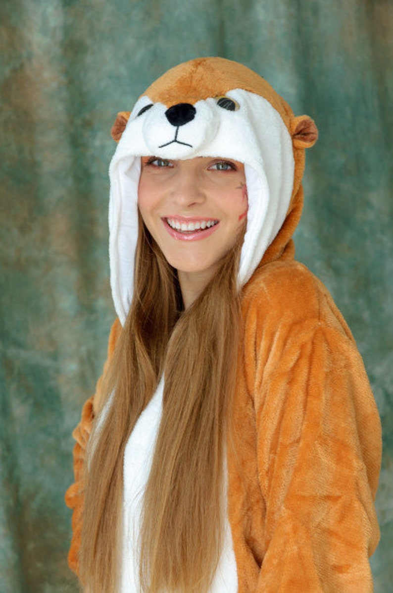 May include: A young person wearing a brown and white furry animal costume with a long, blonde ponytail. The costume has a large, round head with a white face and black eyes. The person is smiling.