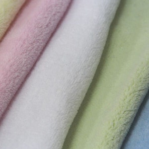 Op de afbeelding: Vijf stofstalen in verschillende kleuren: lichtgeel, roze, wit, lichtgroen en lichtblauw. De stof is zacht en pluche, met een pluche textuur.