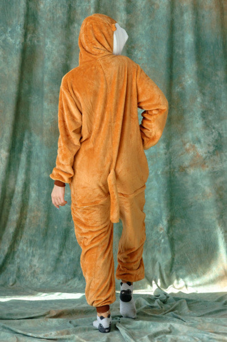 May include: A brown hooded jumpsuit with a white hood lining. The jumpsuit has a long tail and is made of a soft, plush material.
