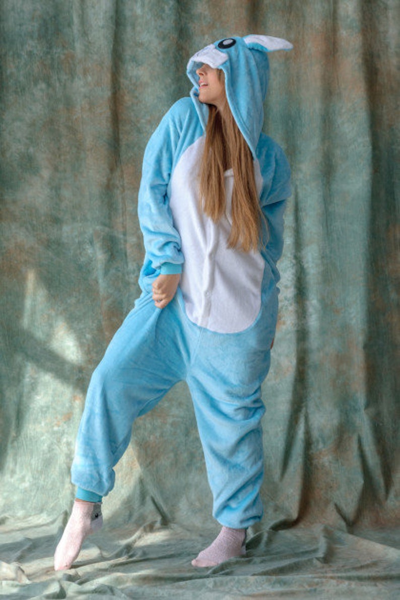 May include: A person wearing a light blue hooded onesie with a white belly and bunny ears. The onesie is made of soft, plush fabric.