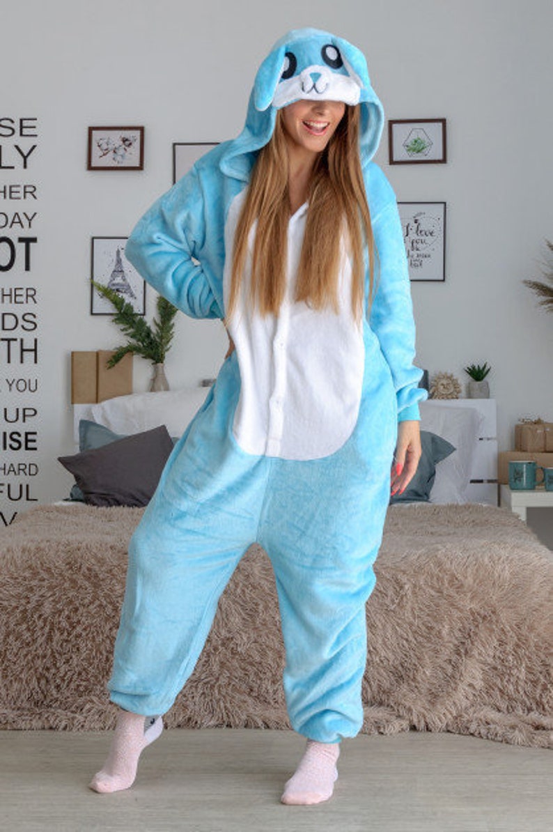 May include: A light blue bunny onesie with a white belly and a hood with bunny ears. The onesie has a zip down the front and a white button at the neck.