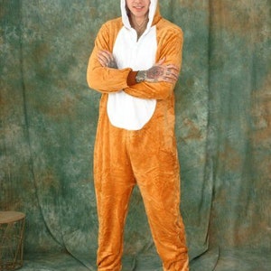 May include: A person wearing a brown and white animal onesie with a hood. The onesie has a cartoon animal face on the hood. The person is wearing yellow animal paw slippers.