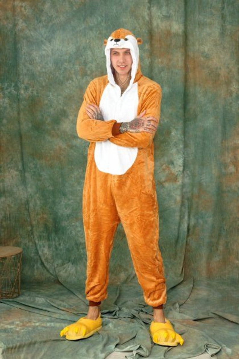 May include: A person wearing a brown and white animal onesie with a hood. The onesie has a cartoon animal face on the hood. The person is wearing yellow animal paw slippers.