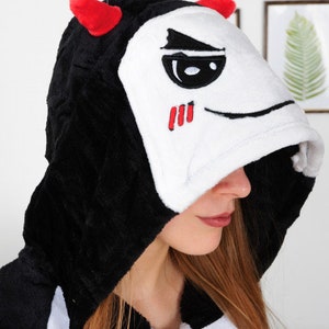 Op de afbeelding: Zwart-witte hooded onesie met rode hoorns en een wit gezicht met zwarte ogen en een rode mond.