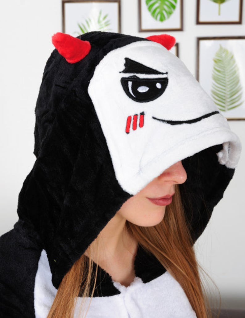 Op de afbeelding: Zwart-witte hooded onesie met rode hoorns en een wit gezicht met zwarte ogen en een rode mond.
