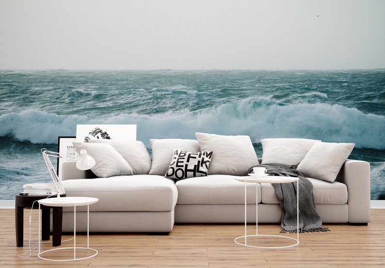 May include: A white sectional sofa with gray throw blankets and pillows. The sofa is in front of a wall mural depicting a stormy ocean with large waves.