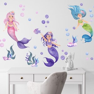 May include: Three mermaid wall decals with purple, pink, and green tails. The mermaids are surrounded by bubbles and seaweed.