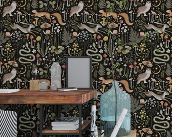 May include: A black and white wallpaper featuring a repeating pattern of woodland creatures, plants, and mushrooms. A wooden desk with a black metal frame and shelves is positioned in front of the wallpaper. A clear glass vase containing blue liquid sits on the desk. A black and white striped chair is placed next to the desk.