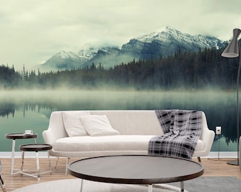 May include: A living room interior with a white sofa, a black and white throw blanket, a round coffee table, and two side tables. The wall behind the furniture features a scenic mural of a lake with fog and mountains in the background.