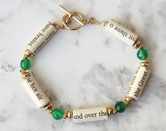 May include: A gold chain bracelet with green gemstone beads and white paper beads with text from a book. The text on the beads reads "have coura have brains, The hot air And over the ont there o ful and wo the Great".
