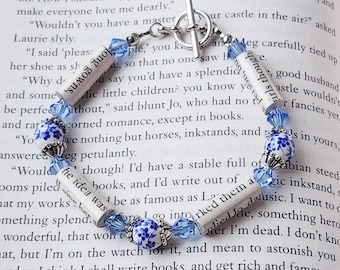 May include: A blue and white charm bracelet with a silver clasp. The bracelet features several charms, including a blue and white floral charm, a blue glass bead, and a rolled-up piece of paper with the text "Sumos Quon" written on it.