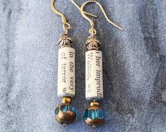 May include: Gold dangle earrings with blue glass beads and a white paper scroll with the text "ther imprud Watson, we in the very terror w"