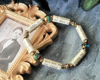 May include: A bracelet made of rolled up pages of a book with gold beads and turquoise blue glass beads. The text on the pages reads "A hundred" and "Which mus".
