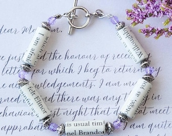 May include: A silver charm bracelet with purple beads and small rolled paper charms with text from a book. The text on the charms reads "I am afraid which are", "Otégé, as you", and "his usual tim nel Brandon".