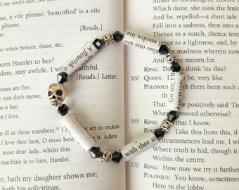 May include: A black and silver skull charm bracelet with black beads and paper scrolls. The scrolls have text from Shakespeare's Hamlet, including the lines "I will o'ersway't" and "with thee ain't."