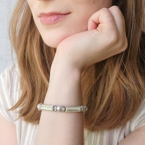 May include: A bracelet made of a book page with small pearl-like beads and silver accents. The bracelet reads "Nay, if you are a villain in the matter, you must needs be a villain of the first magnitude, and I have a villainous suspicion that you are so."