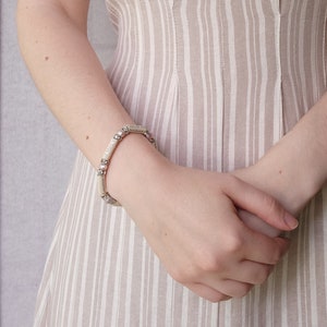 May include: A silver bracelet with small round beads and rectangular links. The bracelet is worn on a person's wrist.