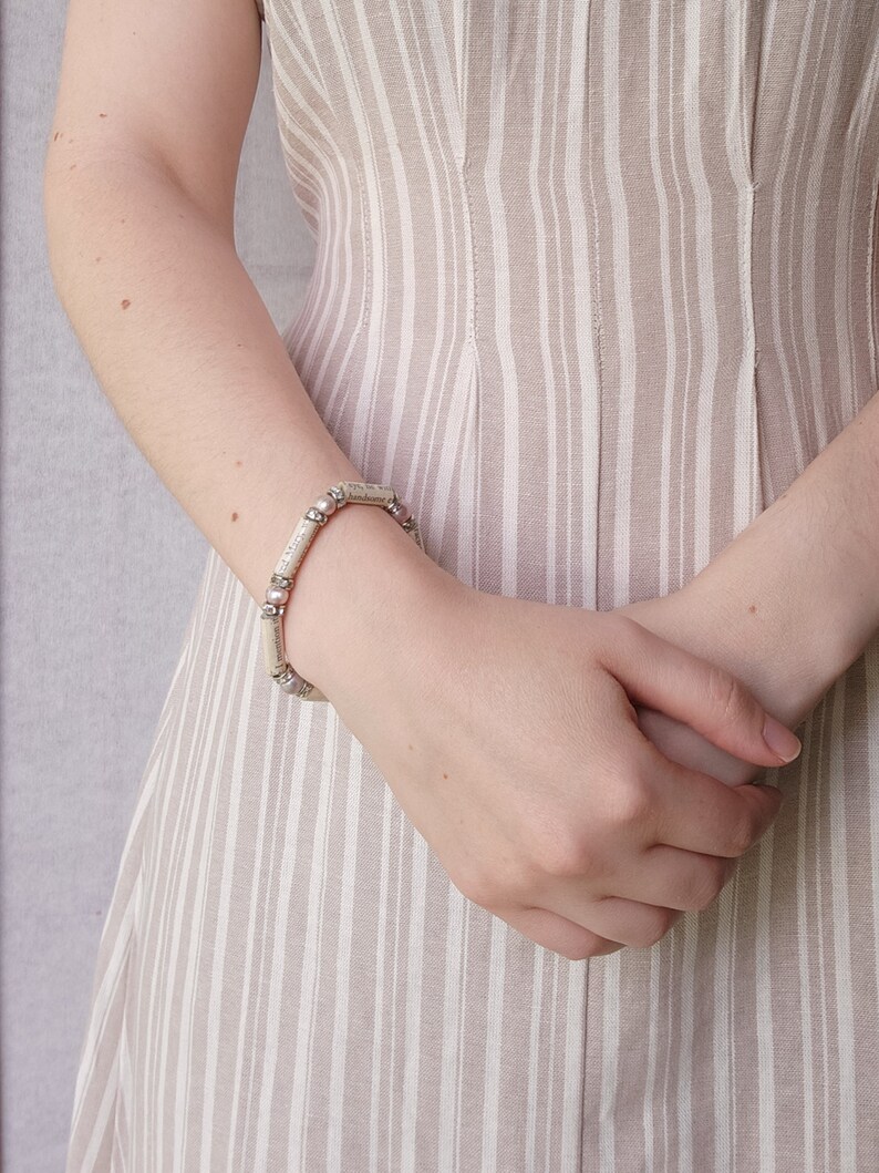 May include: A silver bracelet with small round beads and rectangular links. The bracelet is worn on a person's wrist.