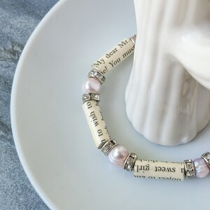 May include: A bracelet made of small white beads with pink accents and silver accents. The beads are made of paper with text printed on them. The text reads "My dear Mr. ... a sweet girl. ... to wish to ... with her h ... e! You must".