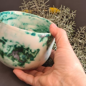 May include: A white ceramic bowl with a green and silver glaze. The bowl has a rounded shape and a wide rim.