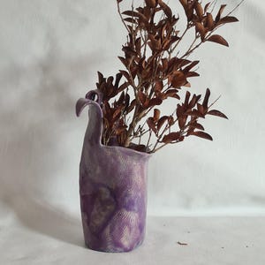 Peut inclure: Un vase en céramique violet avec une forme organique unique et une surface texturée. Des feuilles brunes séchées sont disposées dans le vase.