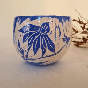 以下が含まれることがあります： 青と白の花柄の陶器のボウル。ボウルは丸みを帯びた形で、様式化された花と葉の模様で装飾されています。青いデザインは白い背景に配置されています。