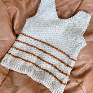 May include: A crocheted tank top with brown stripes on a cream background.