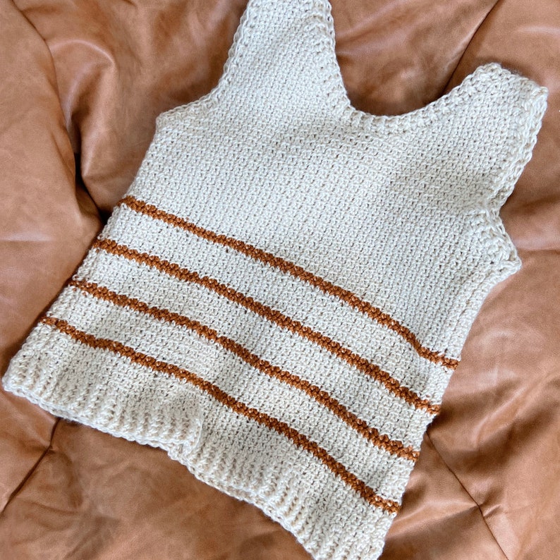 May include: A crocheted tank top with brown stripes on a cream background.