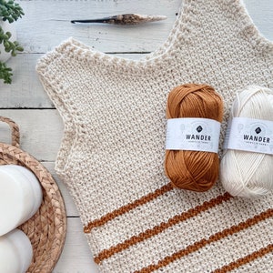 May include: A crocheted sleeveless top with brown and white stripes. The top is made with a beige yarn and has a brown yarn for the stripes. Two balls of yarn are shown, one beige and one brown, with the label "Wander Acrylic Yarn" on each.