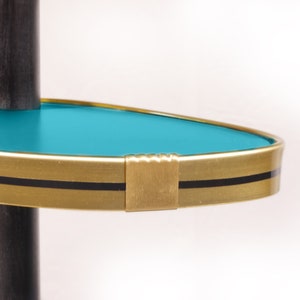 Op de afbeelding: Een turquoise plank met een gouden rand en een zwarte streep. De plank is bevestigd aan een zwarte paal.