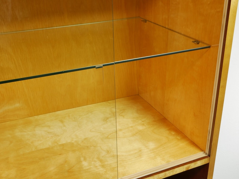 May include: A light-colored wooden display cabinet with glass shelves and a glass door. The cabinet has a simple, minimalist design with clean lines and a natural wood grain finish. The shelves are supported by metal brackets.