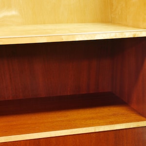 May include: Wooden cabinet with shelves. The cabinet has a light-colored wood frame and shelves, with a darker wood interior. The shelves are rectangular and provide storage space. The cabinet is likely used for displaying or storing items.