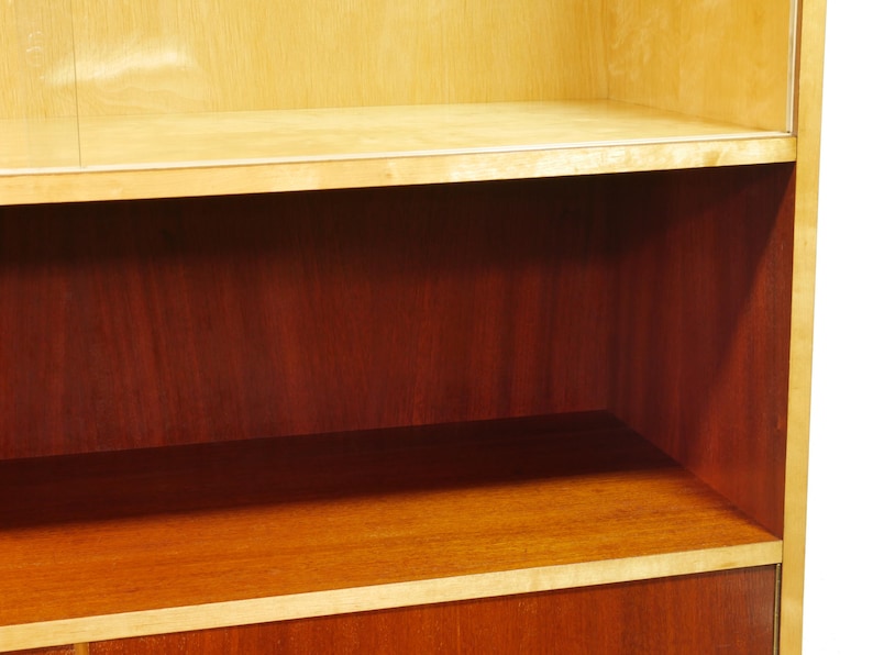 May include: Wooden cabinet with shelves. The cabinet has a light-colored wood frame and shelves, with a darker wood interior. The shelves are rectangular and provide storage space. The cabinet is likely used for displaying or storing items.