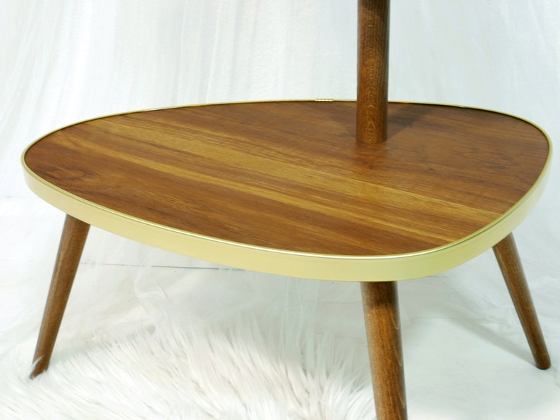 May include: A mid-century modern side table with a wood top and gold trim. The table has three legs and a rounded, oval-shaped top.