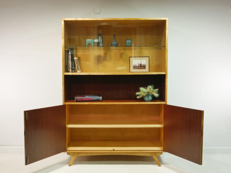 May include: A mid-century modern wooden cabinet with open doors. The cabinet has a light wood finish with a dark wood interior. It features shelves, a glass display area, and decorative items.