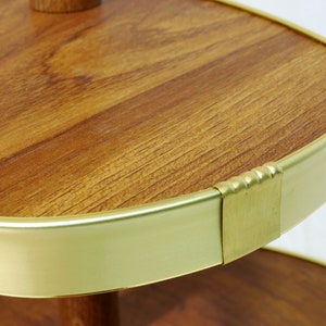 May include: A two-tiered serving tray with a round, wooden top and a gold metal rim. The top tier has a slightly oval shape and the bottom tier is round.