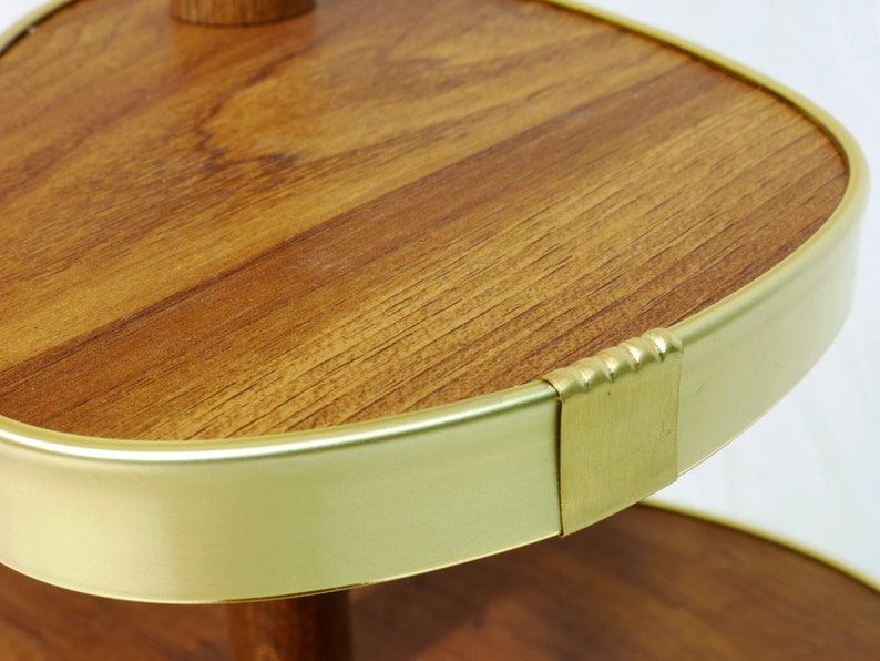 May include: A two-tiered serving tray with a round, wooden top and a gold metal rim. The top tier has a slightly oval shape and the bottom tier is round.