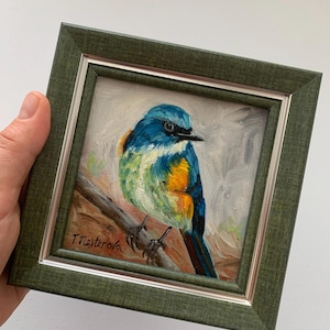 May include: A framed oil painting of a small blue, yellow, and green bird perched on a branch. The painting is signed "T. Masterova" in the lower left corner.